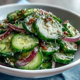 Thin sliced cucumbers, red onion, and dill in tangy vinegar dressing, garnished with sesame seeds.