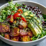 A close-up of a Sweet Potato and Black Bean Bowl topped with creamy avocado slices and a drizzle of lime dressing.