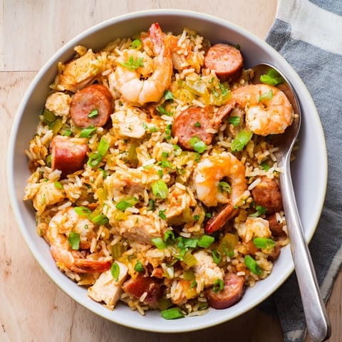 Colorful spoonful of Creole jambalaya revealing tender shrimp, smoked sausage, and chicken amidst spicy tomato sauce.