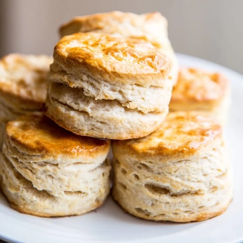 A close up view of golden brown Buttermilk Biscuits showcasing their buttery layers and soft interior, served alongside a jar of fruit jam.