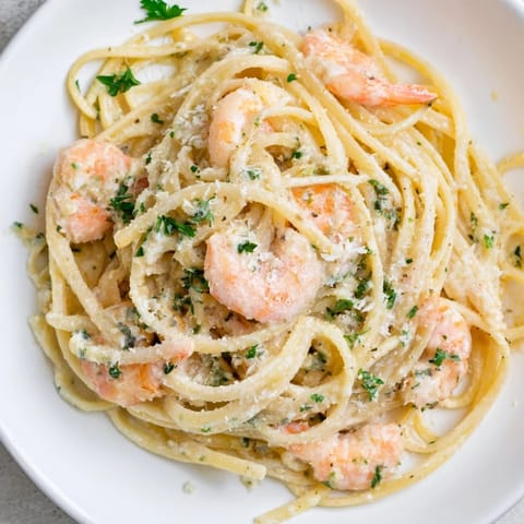 A close-up of Creamy Garlic Shrimp Pasta garnished with fresh parsley, lemon wedges, and a swirl of rich sauce.