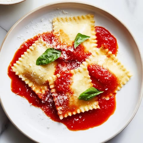 Handmade Spinach Ricotta Ravioli simmering in rich marinara, garnished with fresh basil and grated Parmesan.
