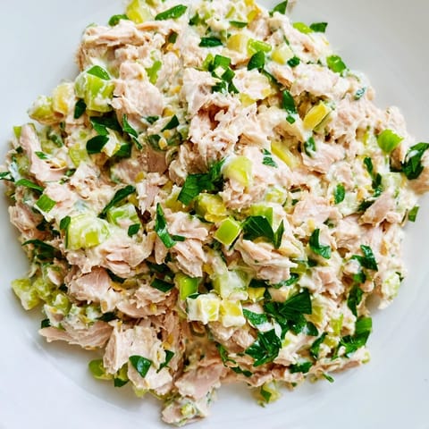A chilled bowl of Spicy Zesty Tuna Salad garnished with lemon wedges and parsley, ready to be scooped onto toasted bread for lunch.