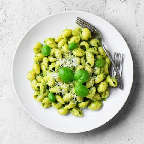 The finished Creamy Avocado Pesto Mac is served in a rustic bowl, topped with extra basil and black pepper for flavor.  