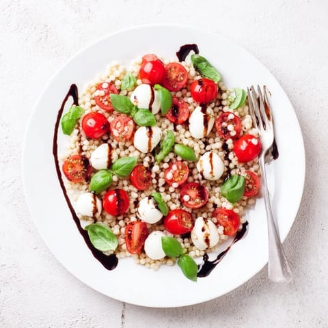A vibrant Caprese Couscous Salad with tender pearl couscous, juicy cherry tomatoes, and creamy mozzarella balls, all tossed in a tangy balsamic glaze.  