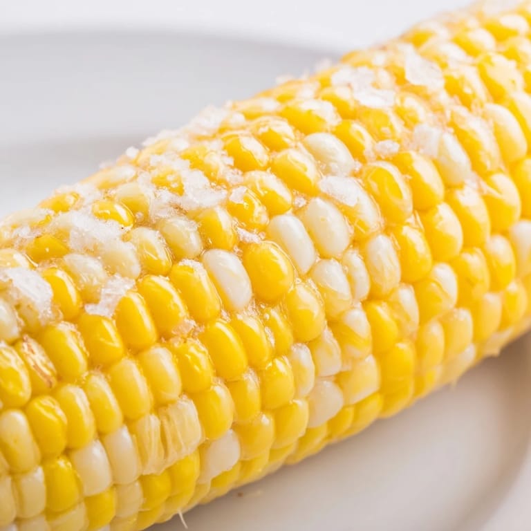 Juicy grilled Corn on the Cob with light char marks, served warm on a rustic wooden cutting board with butter.