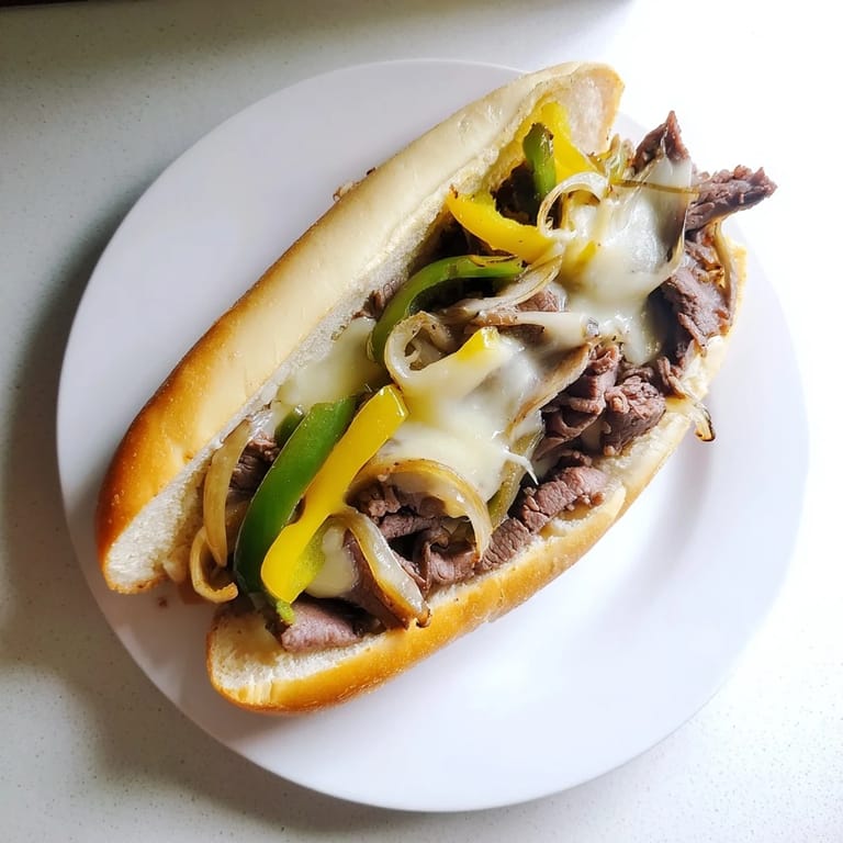 A close-up of a deliciously cheesy and meaty Philly Cheesesteak with sautéed onions on a hoagie.