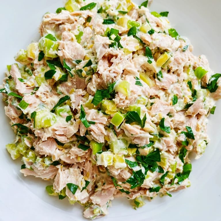 A chilled bowl of Spicy Zesty Tuna Salad garnished with lemon wedges and parsley, ready to be scooped onto toasted bread for lunch.