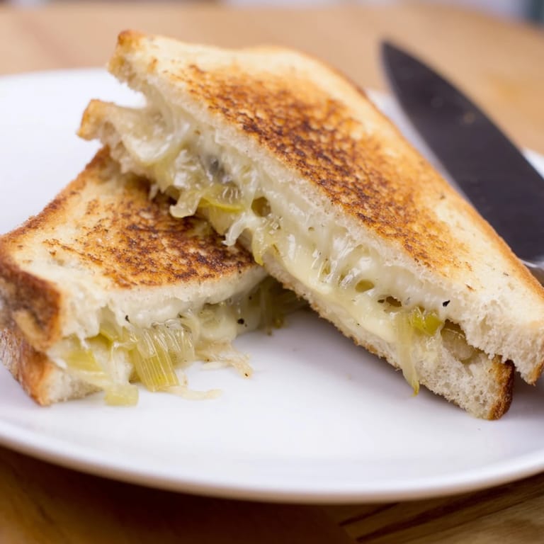 A close-up of crispy Havarti & Caramelized Leek Grilled Cheese, showcasing the sweet, soft leeks and melted Havarti between buttery toasted bread.