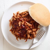 Golden-brown shredded pulled pork sandwich piled high with tangy barbecue sauce on a soft toasted bun.