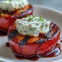 Grilled plums with goat cheese and balsamic glaze on a serving platter with fresh mint garnish for a summer appetizer.