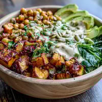 Roasted Sweet Potato and Chickpea Bowl topped with avocado and pumpkin seeds on a rustic wooden table.