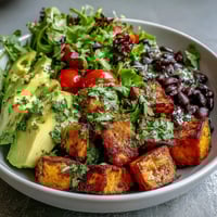 Overhead view of a Sweet Potato and Black Bean Bowl with roasted veggies, fresh salsa, and sliced avocado over greens.
